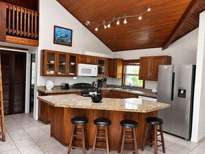 A kitchen with wooden cabinets, a granite countertop, a stainless steel refrigerator, and a bar stool area. - 3bed treat in West End with A/C, WiFi, parking. Chief's Haven (Roatan)