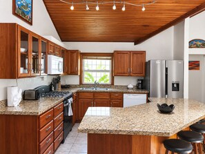 A kitchen with wooden cabinets, a granite countertop, a stainless steel refrigerator, and a window with a view of greenery. - 3bed treat in West End with A/C, WiFi, parking. Chief's Haven (Roatan)