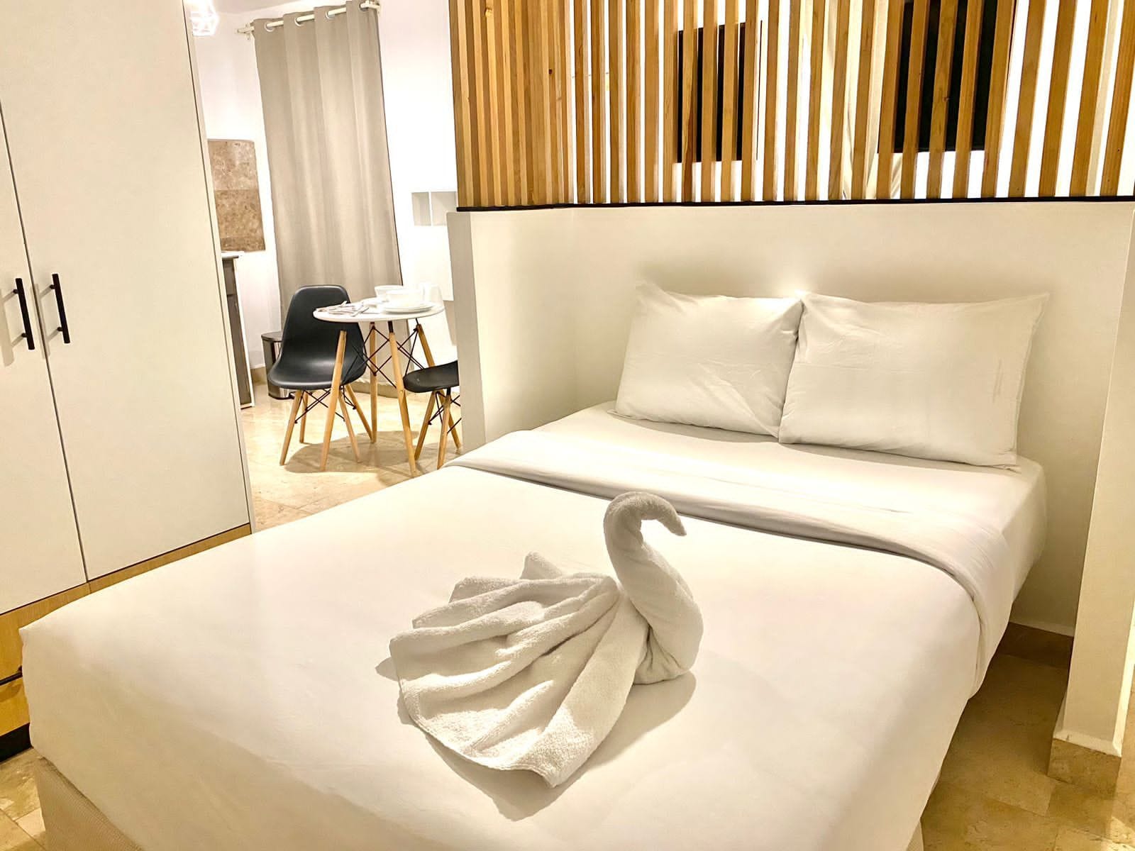 Habitación de hotel con una cama, cabecera de madera, zona de comedor con mesa y sillas, y un armario.