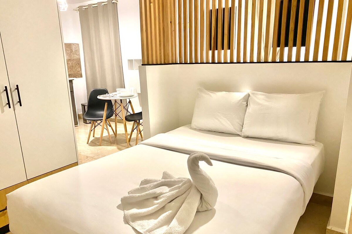 A hotel room with a bed, a wooden headboard, a dining area with a table and chairs, and a wardrobe.
