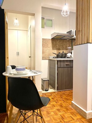 Cocina compacta con comedor, refrigerador, estufa y un pequeño bote de basura.