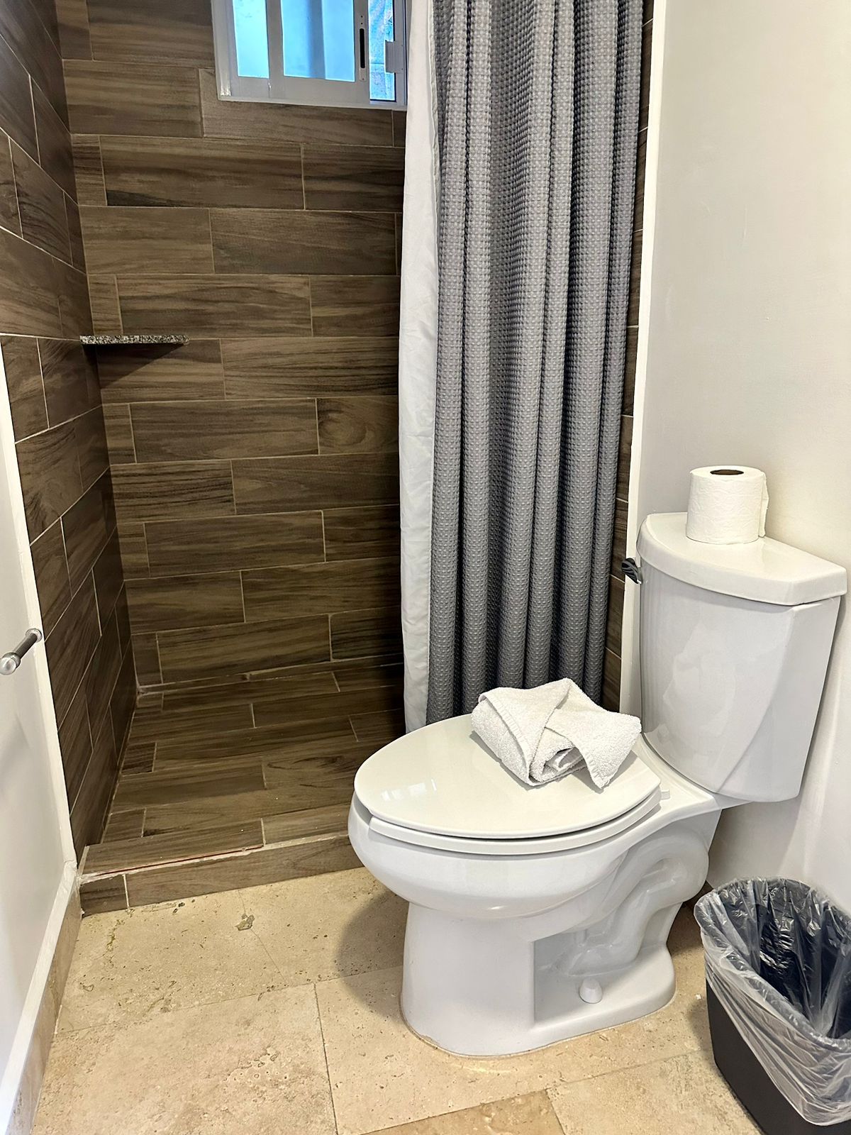 Un baño con inodoro, cortina de ducha y un cubo de basura.