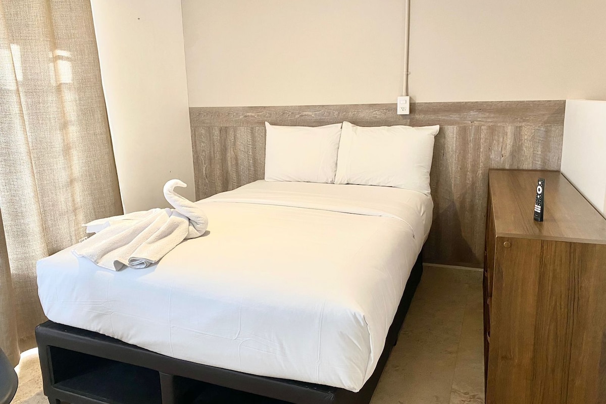 A hotel room with a bed, a wooden nightstand, and a remote control on the nightstand.