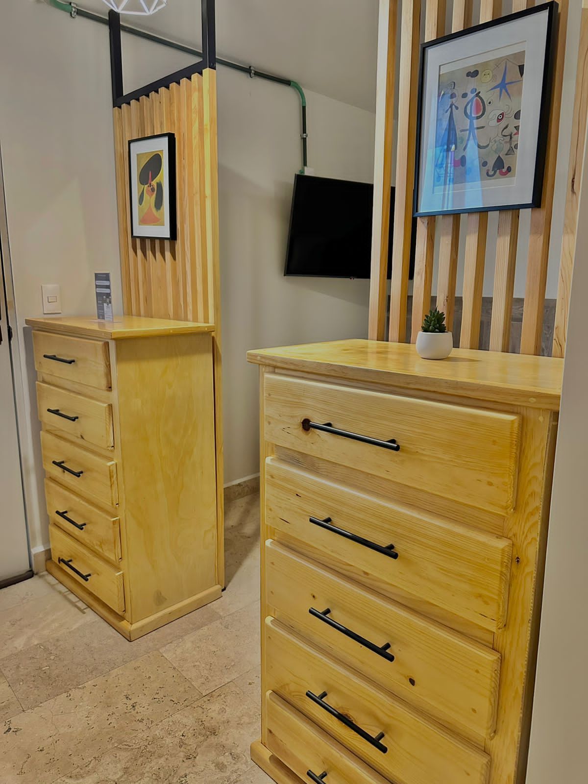 Quarto com cômoda de madeira, televisão de tela plana na parede e quadro emoldurado sobre a cômoda.