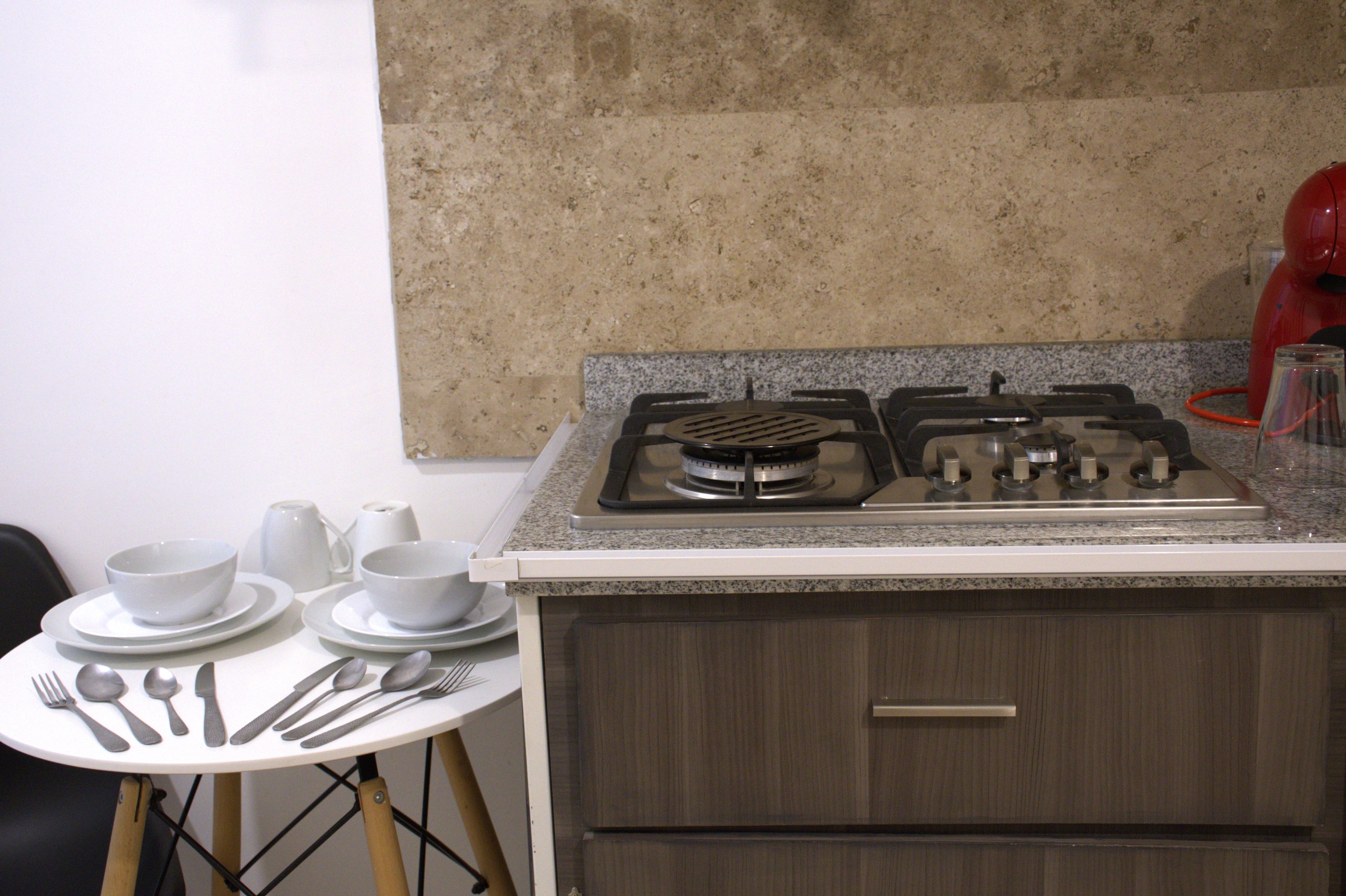 A kitchen with a gas stove, granite countertop, and a dining table set with cutlery and bowls.