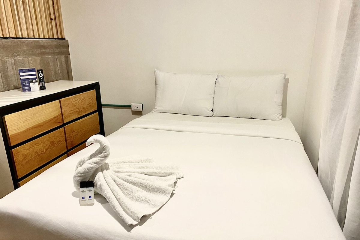 A hotel room with a bed, a wooden dresser, and a towel on the bed.