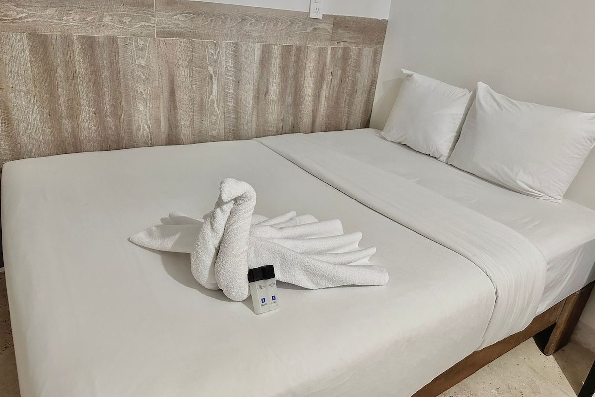 A hotel room with a neatly made bed, a wooden headboard, and a white wall.