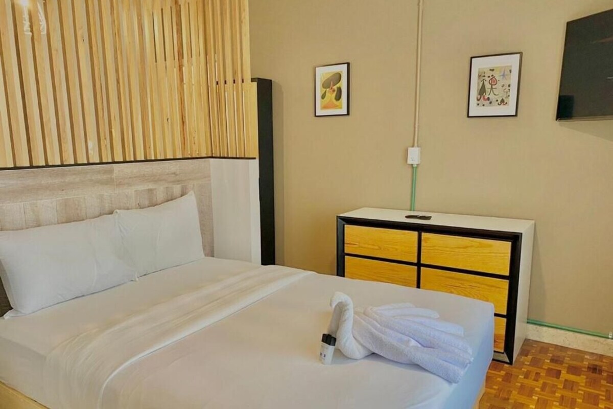 A hotel room with a bed, a bedside table, a wall-mounted TV, and artwork on the wall.