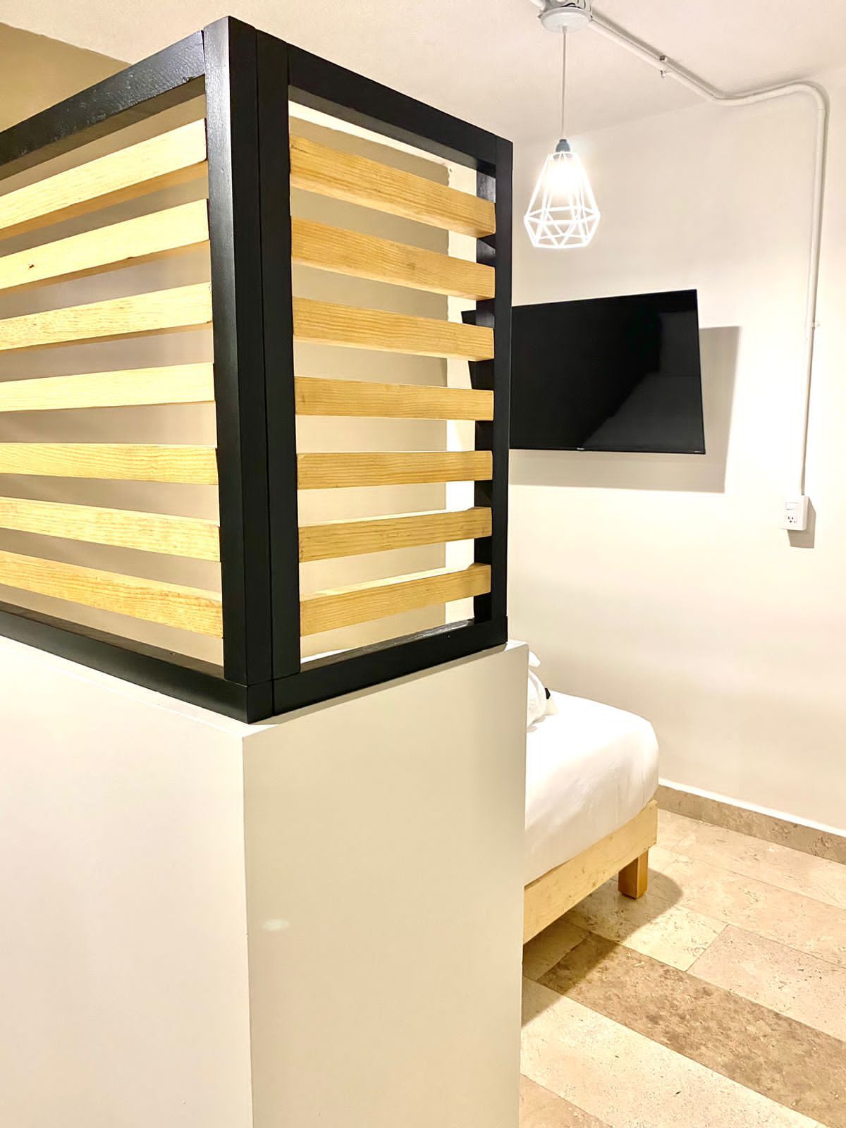 Un dormitorio con cama, televisor montado en la pared y lámpara colgante.