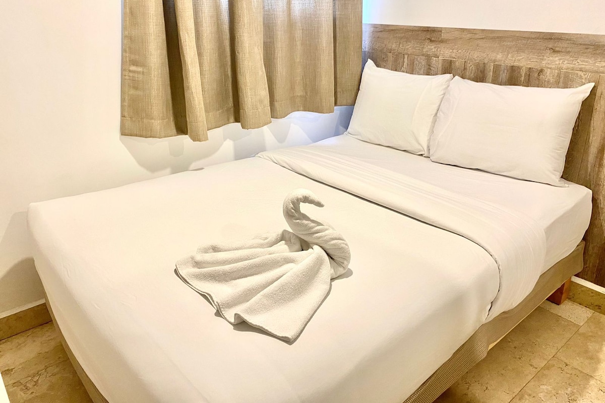 A hotel room with a bed, a wooden headboard, and a window with curtains.