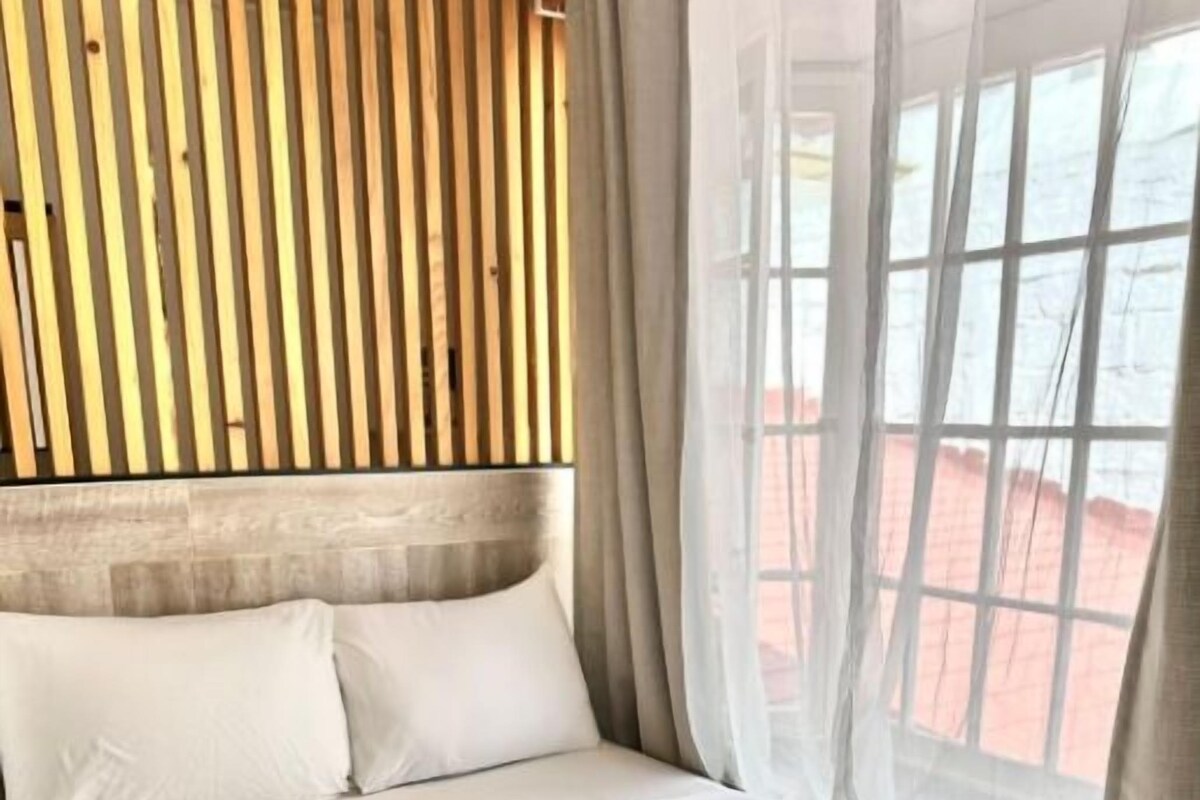 A hotel room with a bed, a wooden headboard, and a window with curtains.