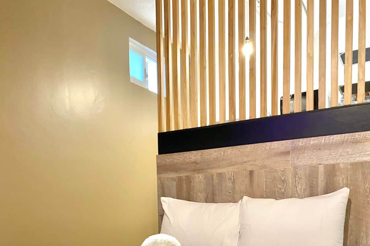 A hotel room with a bed, white pillows, a wooden headboard, and a towel on the bed.