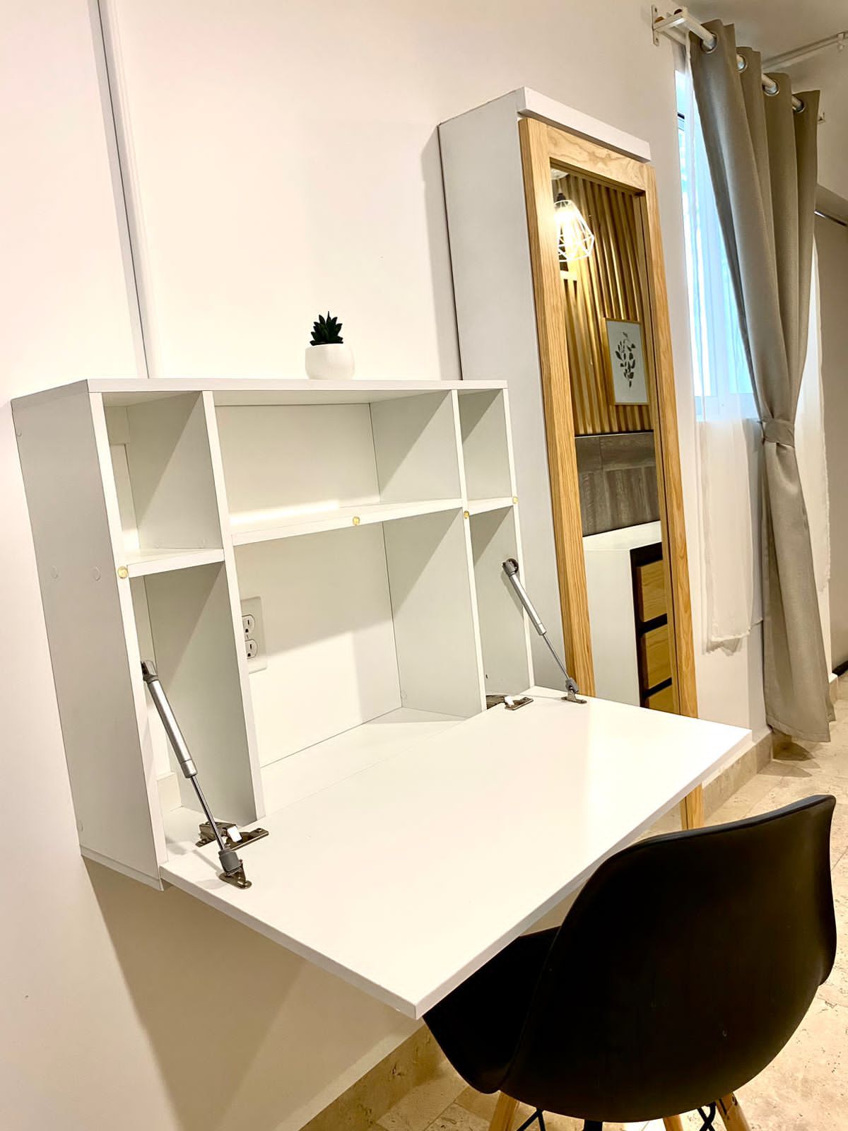Un escritorio blanco con estanterías, una silla negra y un mueble de madera con una planta.