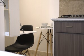 A compact kitchen with a gas stove, a small round table with a bowl, and a black chair. - Tamarindo by Homi Rent (Santiago de Querétaro)