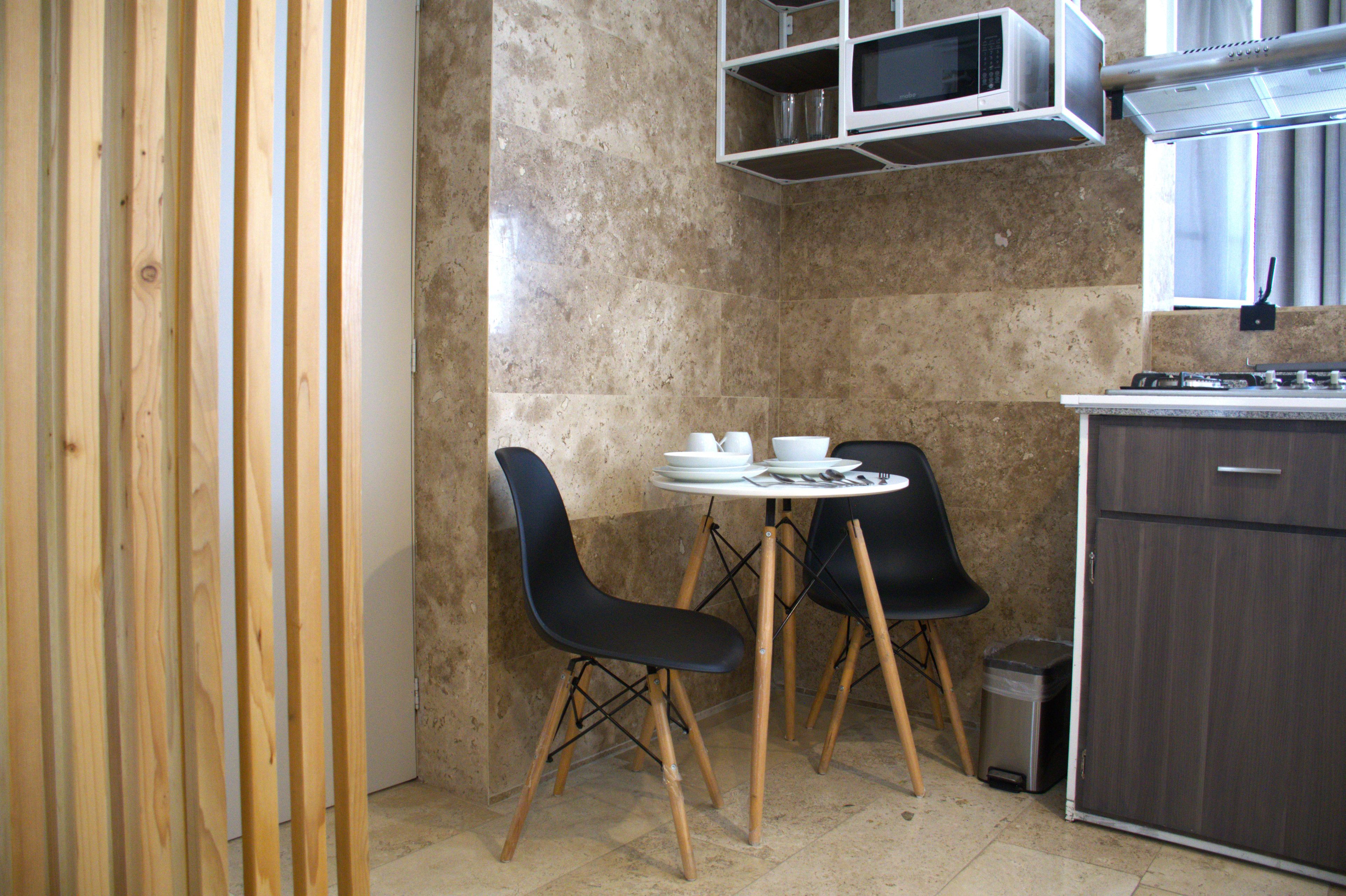 A compact kitchen with a dining table and chairs, a microwave, and a trash bin.