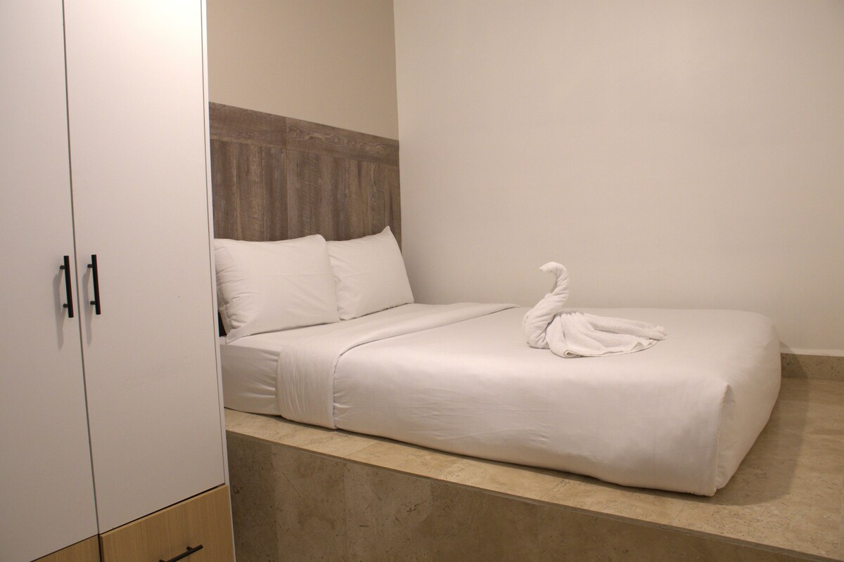 A neatly made bed with a swan-shaped pillow in a room with a wooden headboard and a wardrobe.