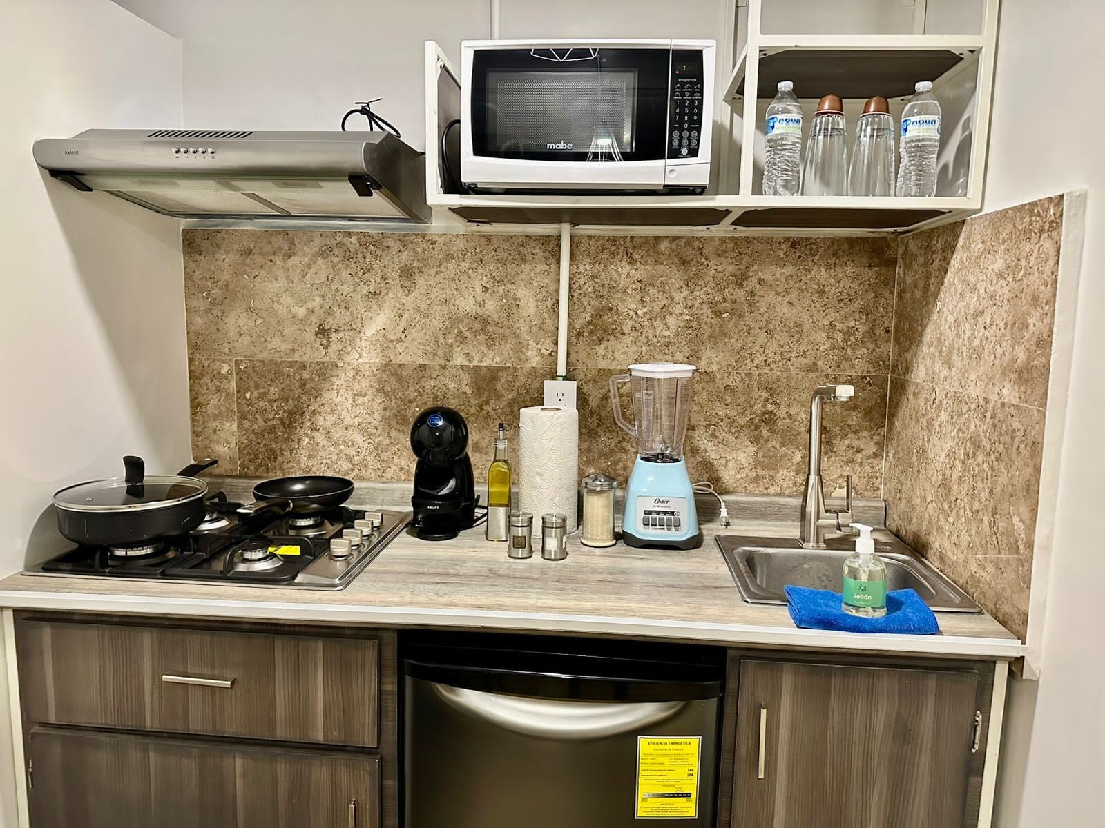 Una cocina con estufa, microondas, licuadora y fregadero.
