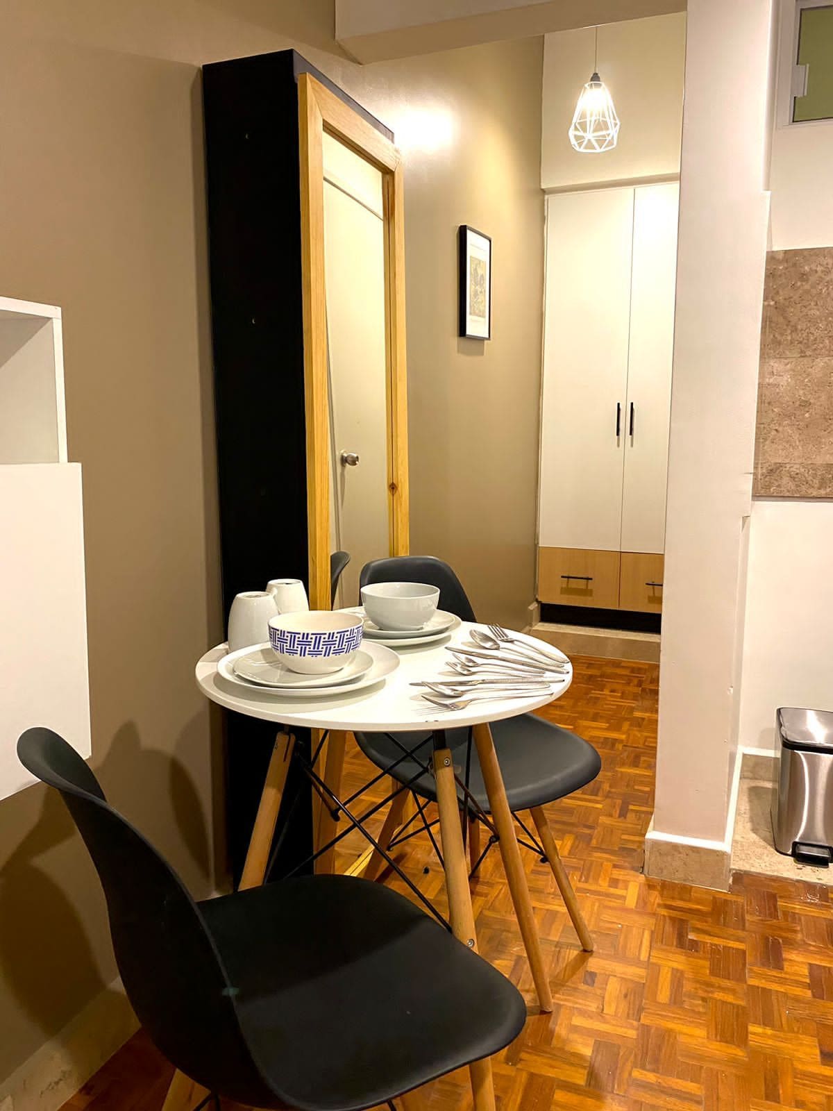 Un espacio de comedor compacto con una mesa redonda, sillas negras y un armario blanco al fondo.