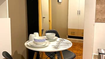 Un espacio de comedor compacto con una mesa redonda, sillas negras y un armario blanco al fondo.