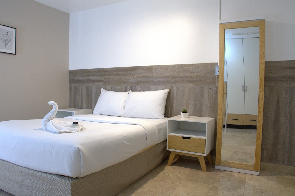 A hotel room with a bed, a nightstand, a mirror, and a wall-mounted picture.