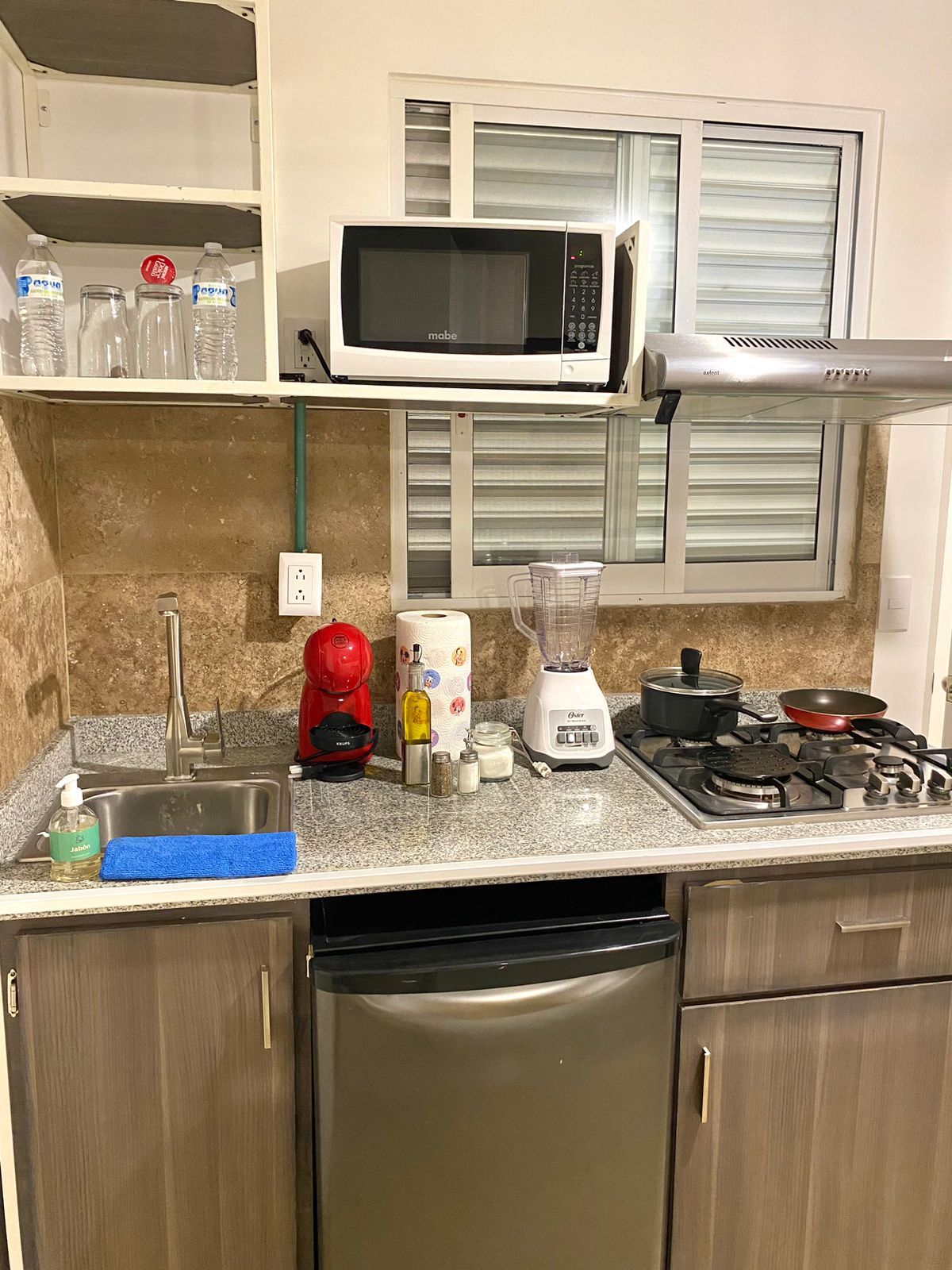 A compact kitchen with a microwave, stove, coffee maker, blender, and a sink.
