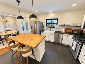 Una cocina moderna con una mesa de comedor de madera, dos lámparas colgantes, electrodomésticos de acero inoxidable y vistas al exterior.