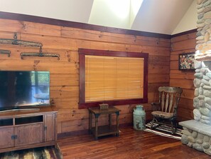 A wooden-paneled room with a television, a stone wall, and a wooden chair. - 4-bedroom PNW Woodland Lodge near Mt. St. Helens (Castle Rock)