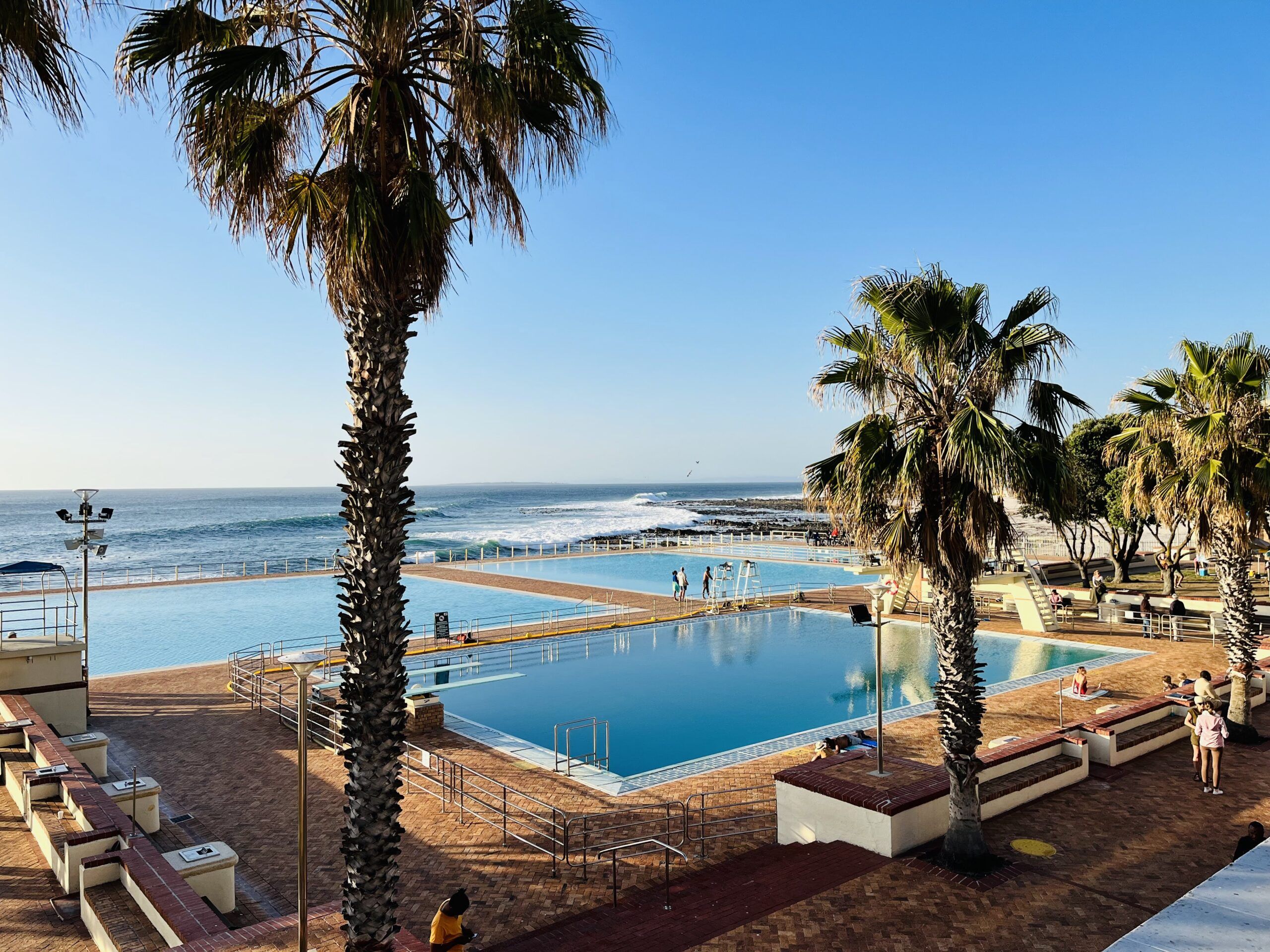 Zona de piscina con vista al océano, palmeras y puesto de salvavidas.