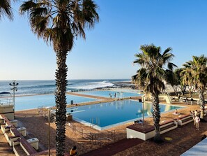 Area piscina con vista sull'oceano, palme e posto di salvataggio.