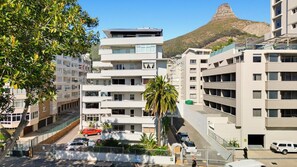 A multi-story residential building with balconies, a parking area, and a mountain in the background. - Luxurious Studio on the Promenade (Cape Town)