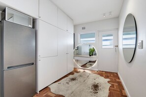 Eine moderne Küche mit einem Edelstahl-Kühlschrank, weißen Schränken, einem runden Spiegel und Holzboden.