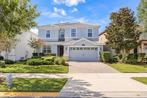 A two-story residential house with a garage, a driveway, and well-maintained landscaping. - ChampionsGate 6BR Pool, Spa & Games (Four Corners)