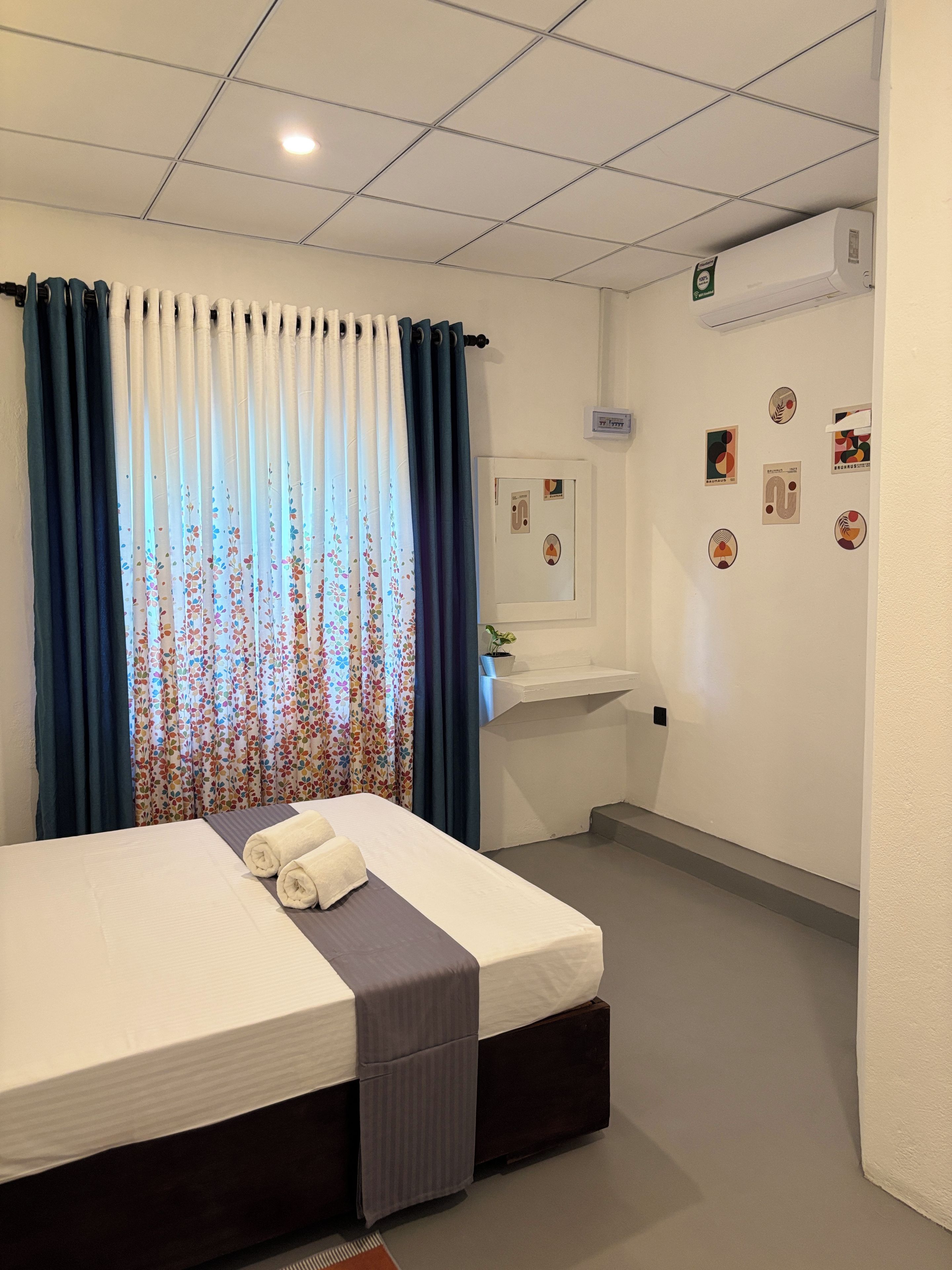 A hotel room with a bed, curtains, a small sink, and wall decorations.