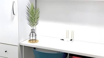 A white desk with a blue chair, a potted plant, and a candle holder.