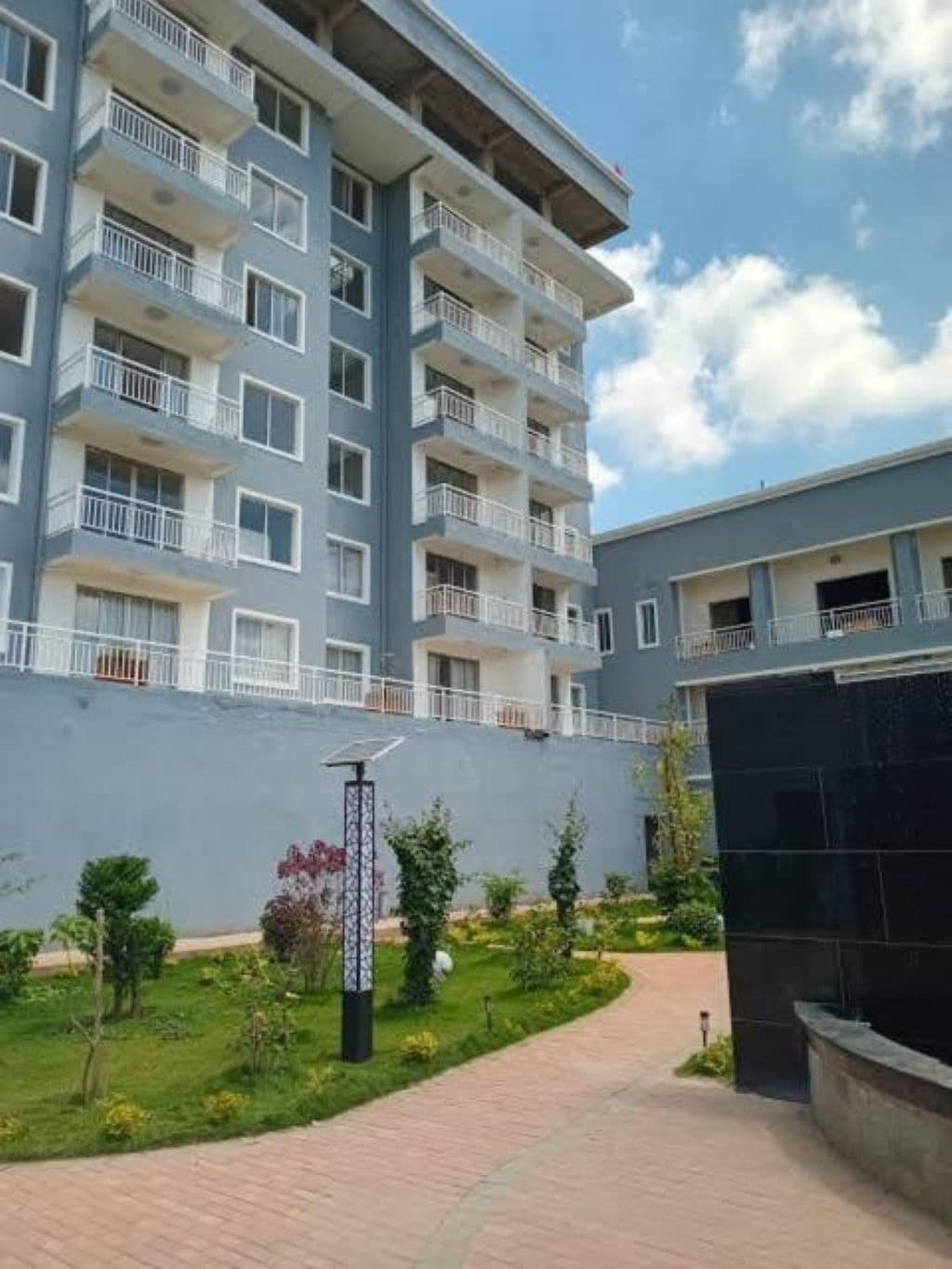 A multi-story residential building with balconies, a paved pathway, and a landscaped garden area.