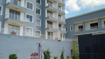 A multi-story residential building with balconies, a paved pathway, and a landscaped garden area.