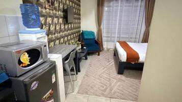 A compact hotel room with a kitchenette, a bed, a desk, and a large window with curtains.