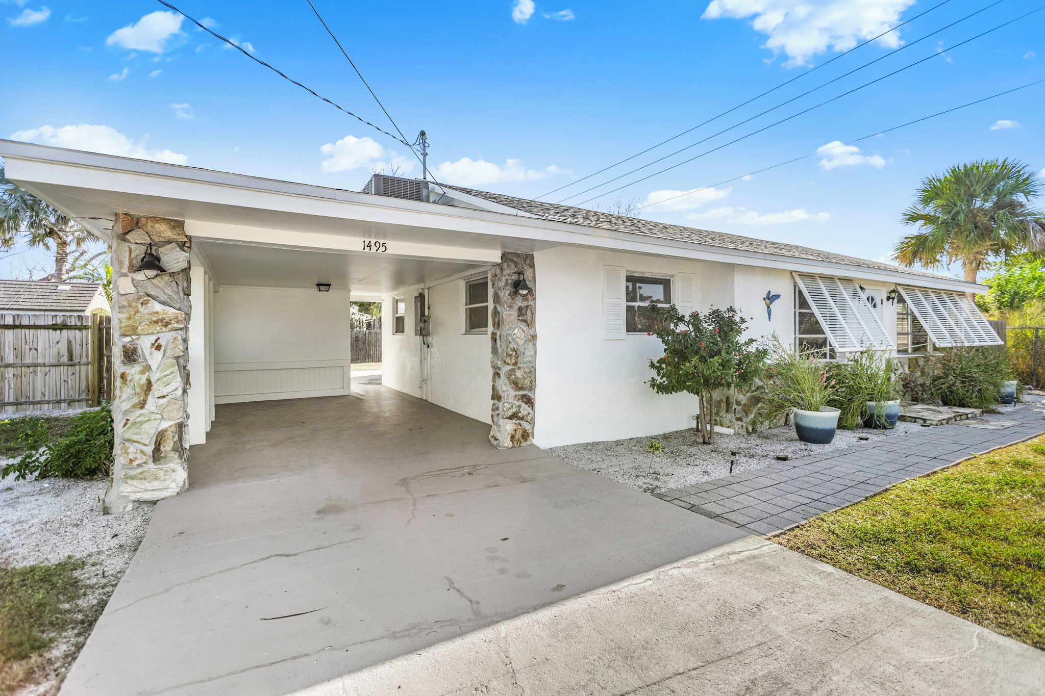 A single-story house with a covered porch, stone pillars, and a number '1495' on the wall.