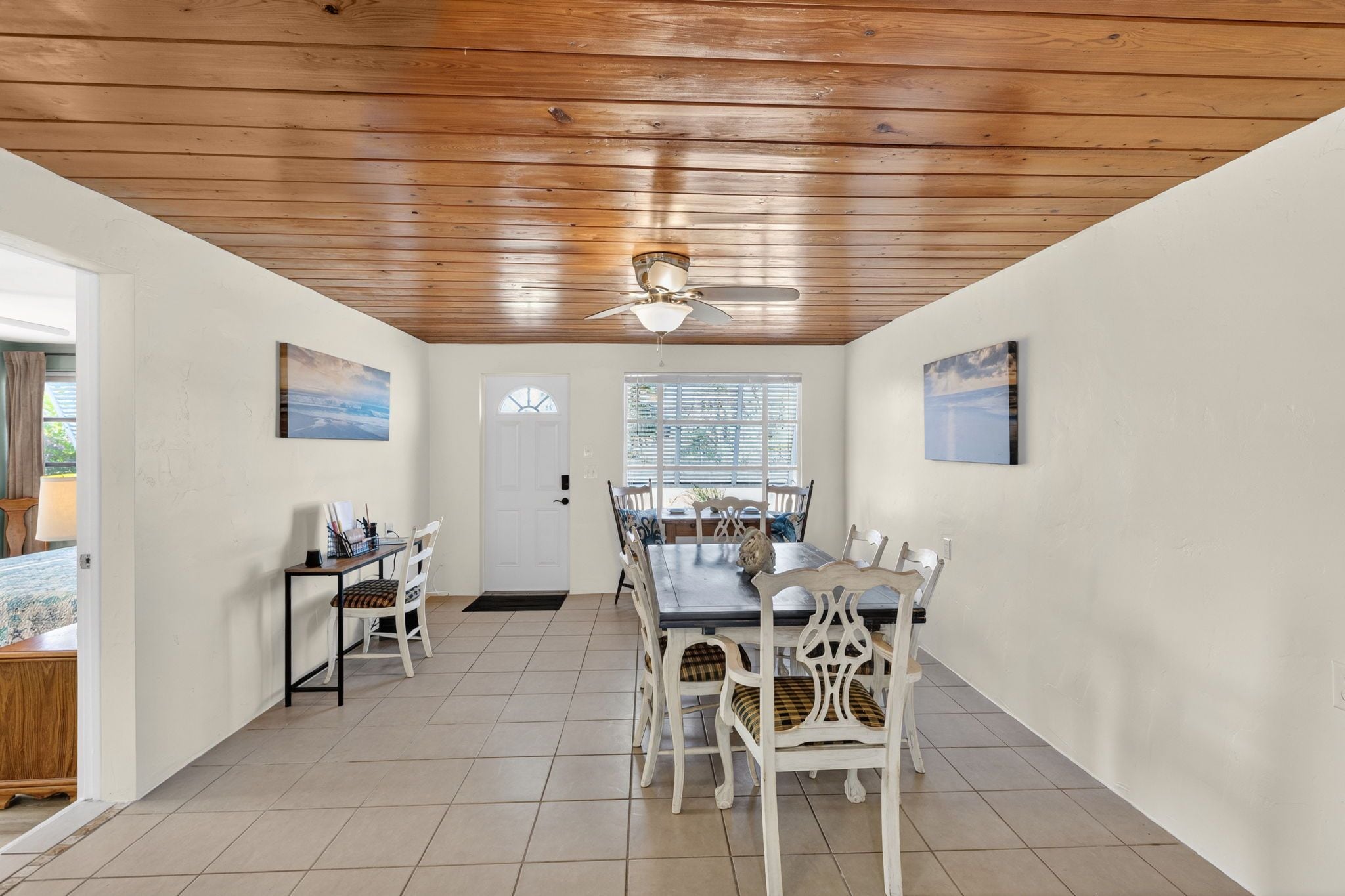 A dining area with a wooden ceiling, white walls, and a large window with blinds.