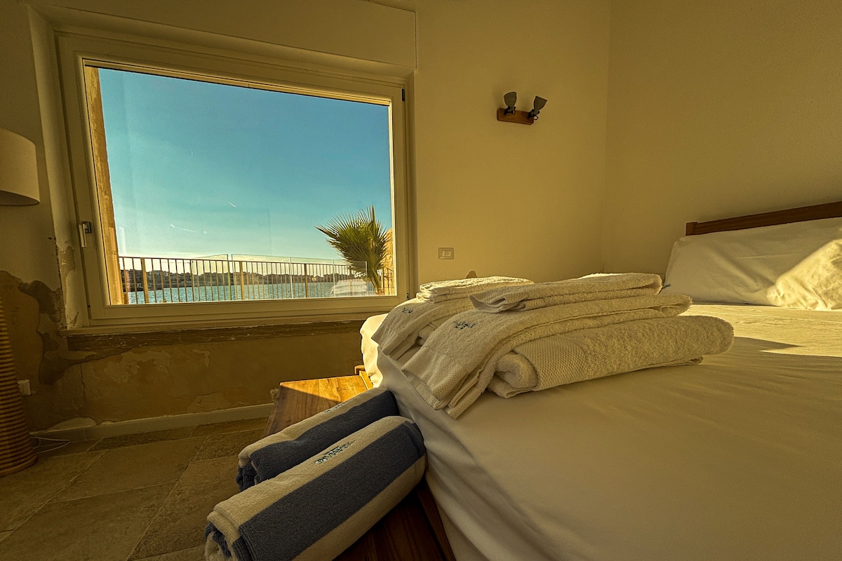 A hotel room with a large window, a bed with neatly folded towels, and a wooden nightstand.