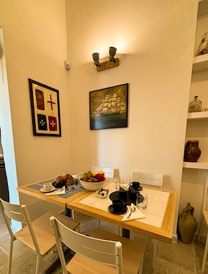 Une table à manger avec des chaises, un saladier rempli de fruits et, au mur, un tableau représentant un navire.