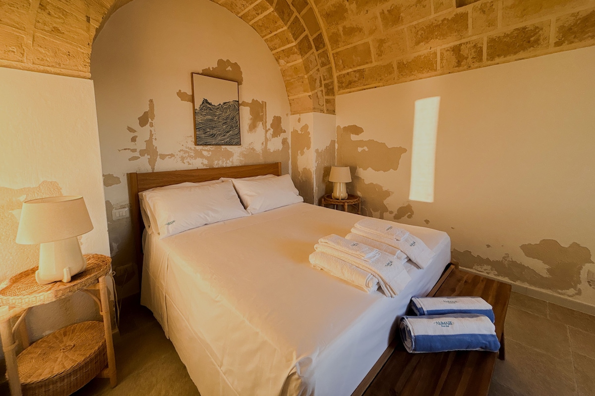 A room with a bed, two bedside tables with lamps, a wall-mounted artwork, and a towel rack with towels.