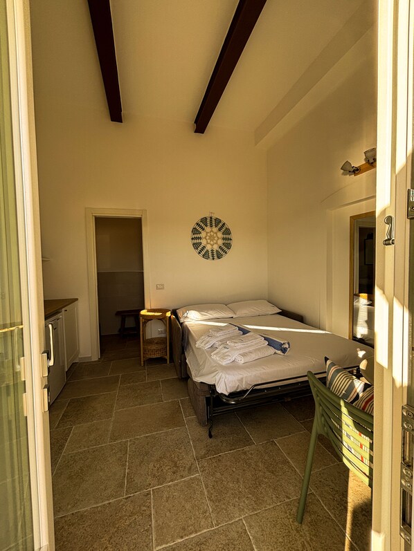 A bedroom with a bed, a bedside table, a wall decoration, and a view of the outside.