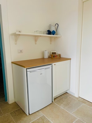 A compact kitchenette with a white refrigerator, a wooden countertop, and a white cabinet. There is a shelf above holding various kitchen items. - Ammare B&B (Trani)