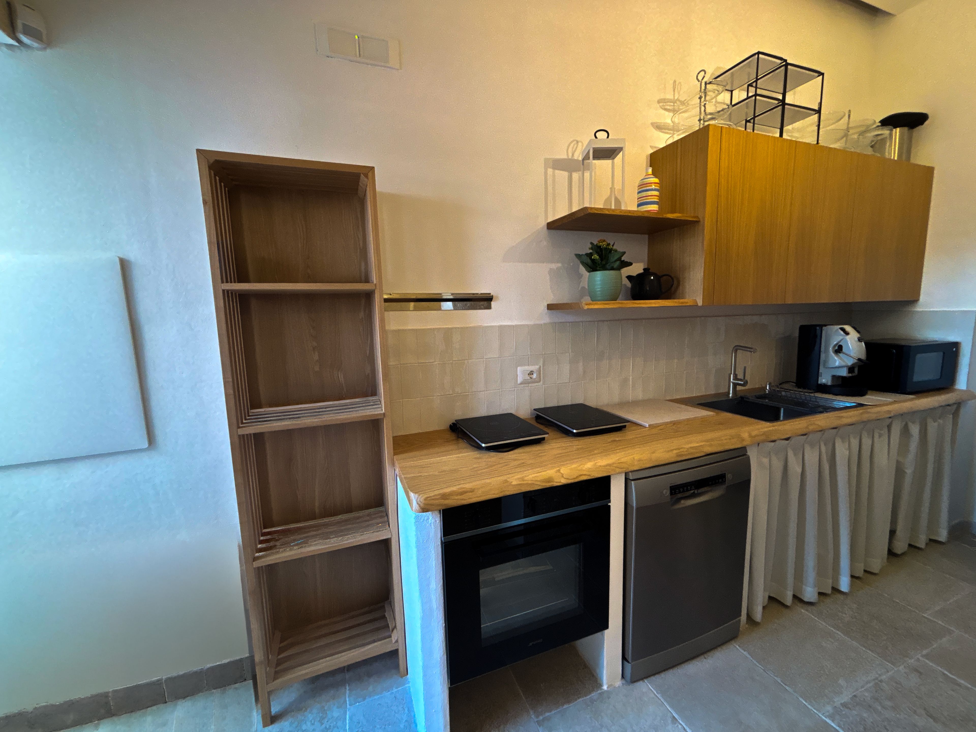 Een compacte keuken met een inbouwoven, een magnetron en een spoelbak. Daarboven bevindt zich een houten plank, waarop een kleine potplant staat.