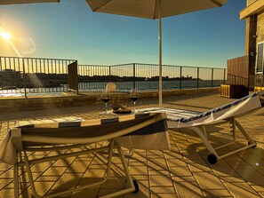 Une terrasse avec une table dressée pour deux personnes, un fauteuil et une vue sur la mer.