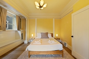 Ett hotellrum med en stor säng, två sänglampor, ett fönster med gardiner och en kristallkrona.
