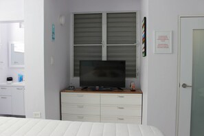 A hotel room with a bed, a television on a dresser, a window with blinds, a door with a sign, and a small table with toiletries. - Casa Iliria 1: cozy 1-bedroom apartment with AC in charming Boquerón (Boquerón)