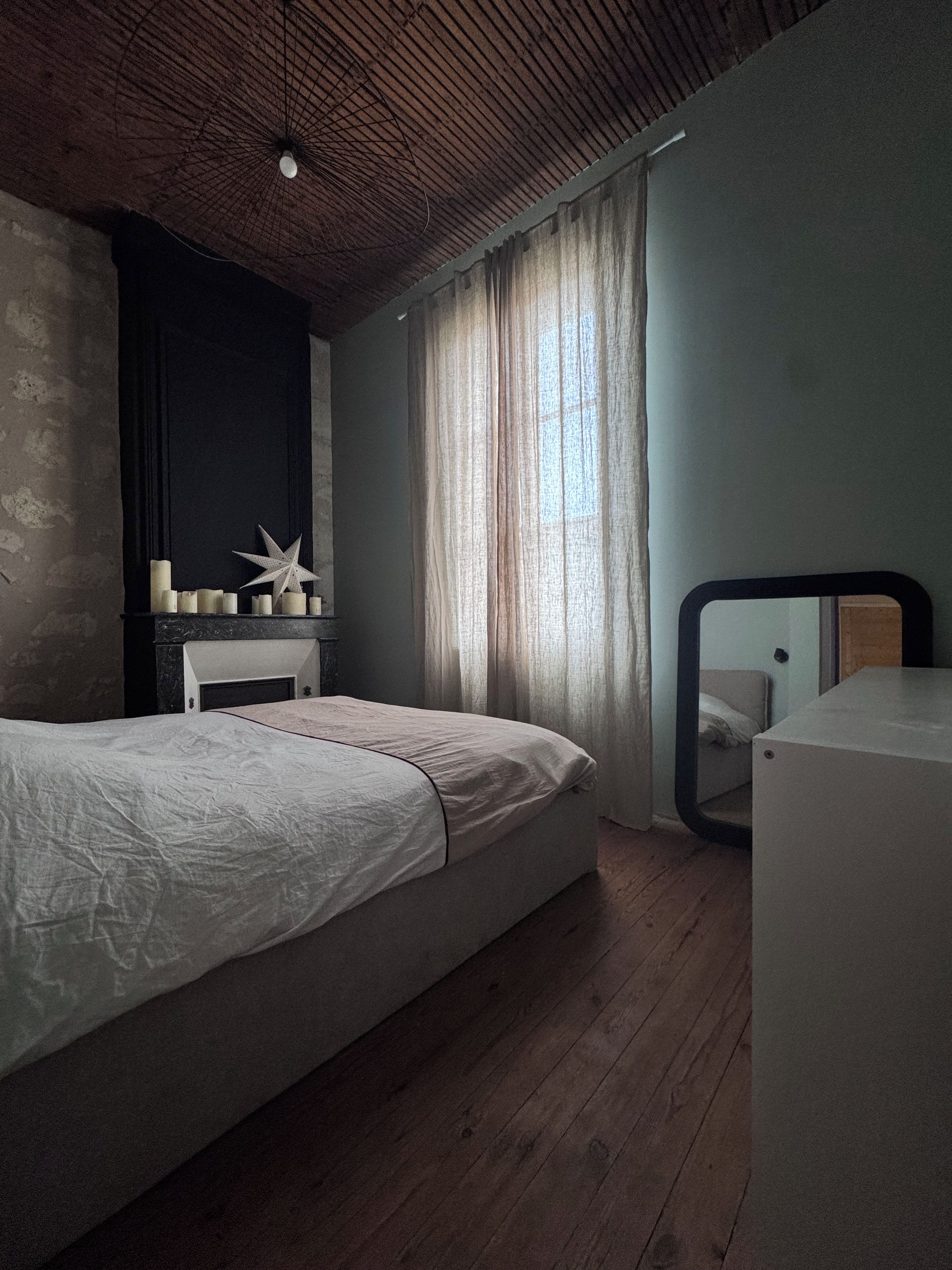 A bedroom with a bed, a dresser, a mirror, and a window with curtains.
