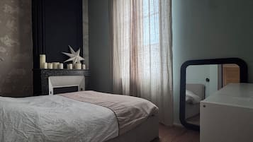 A bedroom with a bed, a dresser, a mirror, and a window with curtains.